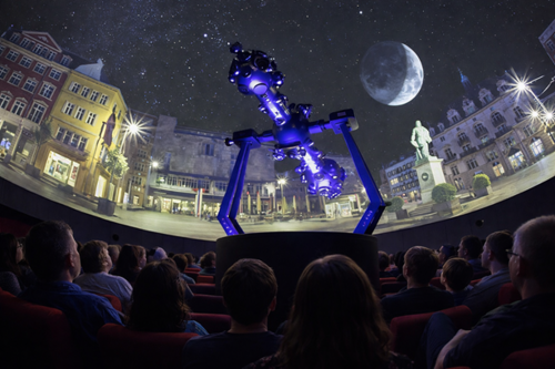 Planetariumspublikum vor blau beleuchtetem Sternprojektor vor Silhouette der Stadt Halle mit Mond im Sternensaal 