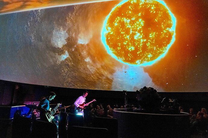 2 Gitarristen mit Sternprojektor vor Planetariumsprojektion einer Sonne