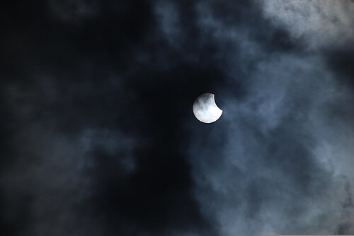 Sonnenfinsternis_Mond bedeckt einen Teil der Sonne bei wolkigem Himmel