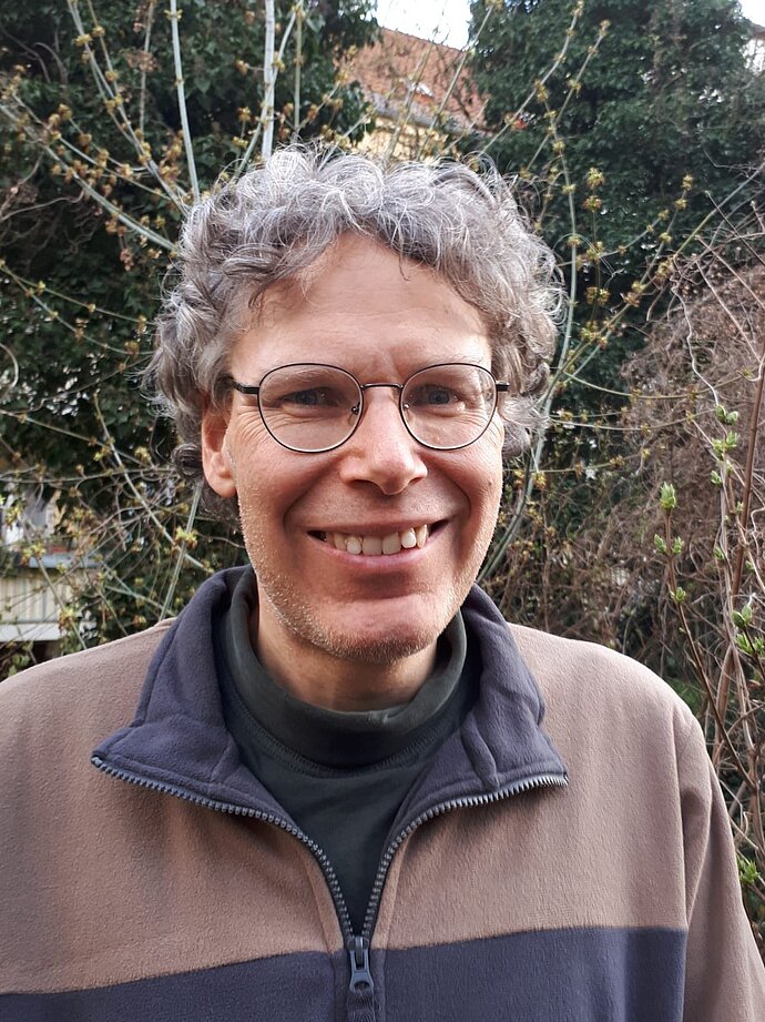 Portrait eines freundlich lächelnden Mannes mittleren Alters mit Brille und lockigen Haaren