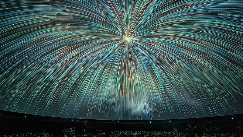 Mit blaugrünen Sternschnuppen, die aus einem hellen Punkt kommen, dicht angefüllte Planetariumskuppel  