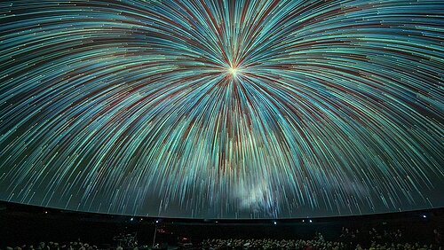Mit blaugrünen Sternschnuppen, die aus einem hellen Punkt kommen, dicht angefüllte Planetariumskuppel  
