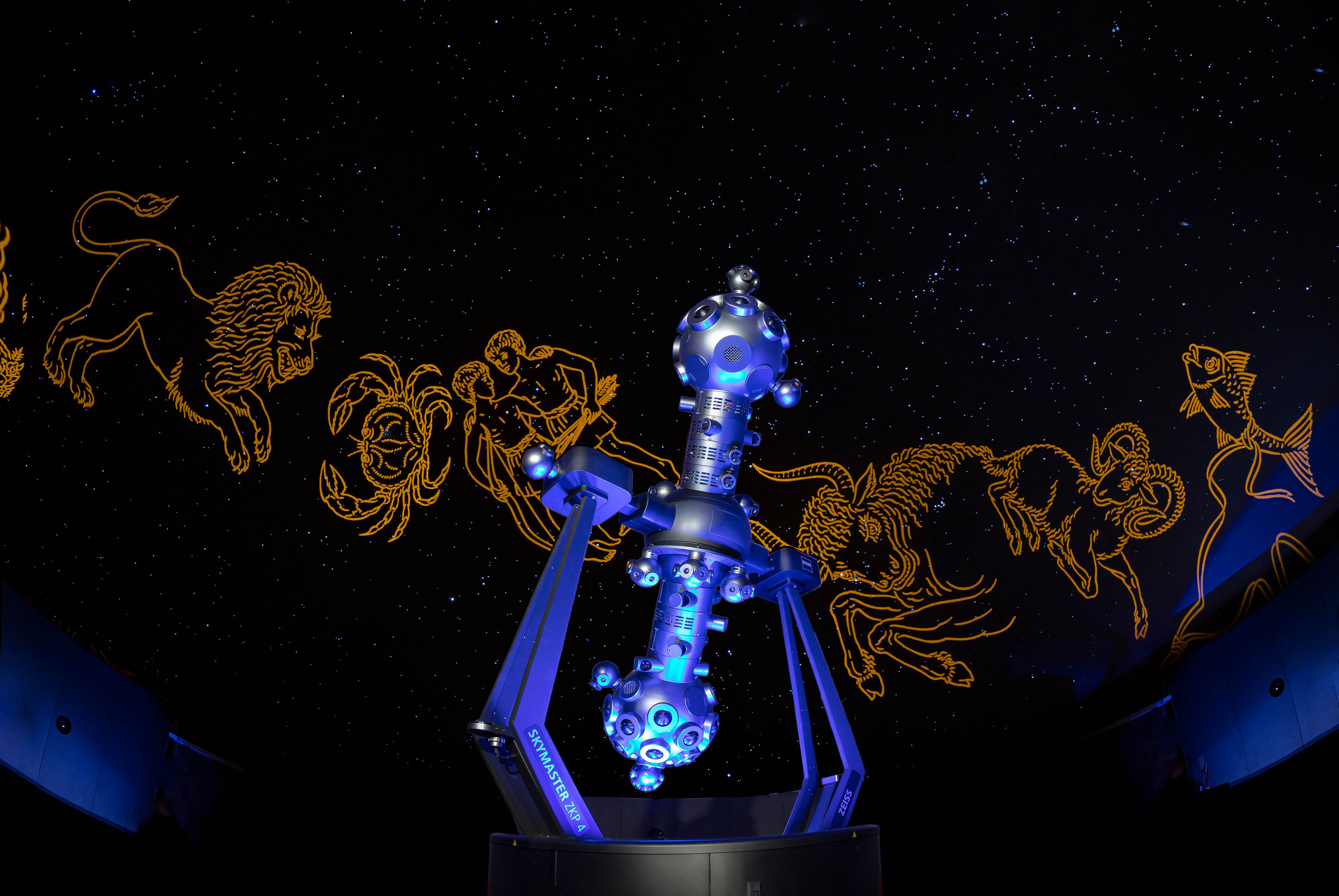 Sternprojektor vor dunklem Sternhimmel mit projizierten Sternbildfiguren in orange Farbe. 