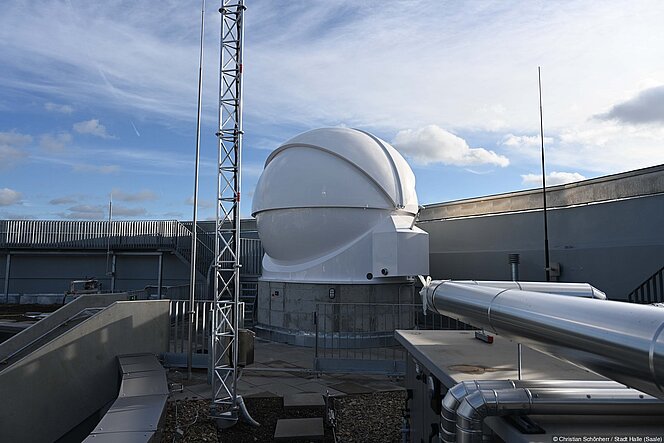 Auf dem Dach des Planetariums leuchtet die weiße Kuppel der neuen Sternwarte vor blauem Himmel.