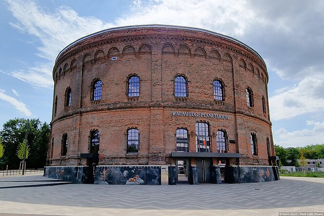 Gesamtansicht des Planetariums Halle vor blauem Himmel mit Jahresband der Sternbilder und fertiggestellten Außenanlagen, Bäumen und Fahrradständern